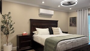 Ein Schlafzimmer mit einem dunkelholzbett, weißer Bettwäsche, einer grünen Tagesdecke, einem Nachttisch mit Lampe, einer Klimaanlage und einem Bild an der Wand.