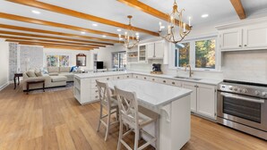 Eine geräumige Küche mit einer großen Kochinsel, Holzbalken, weißen Schränken und einem eingebauten Ofen.