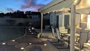 Un patio al aire libre con un espacio de estar techado, una chimenea y luces colgantes.