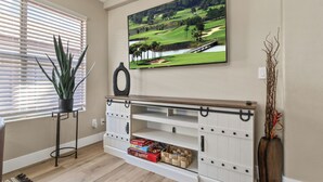 Sala de estar con televisor montado, mueble de madera para entretenimiento y una planta junto a la ventana.