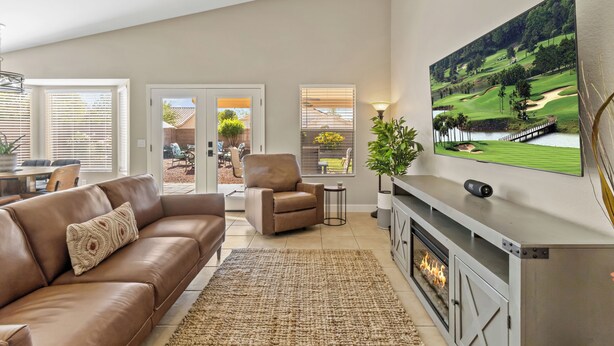 Una sala de estar moderna con un sofá de cuero, una chimenea y un televisor grande montado en la pared mostrando un campo de golf.