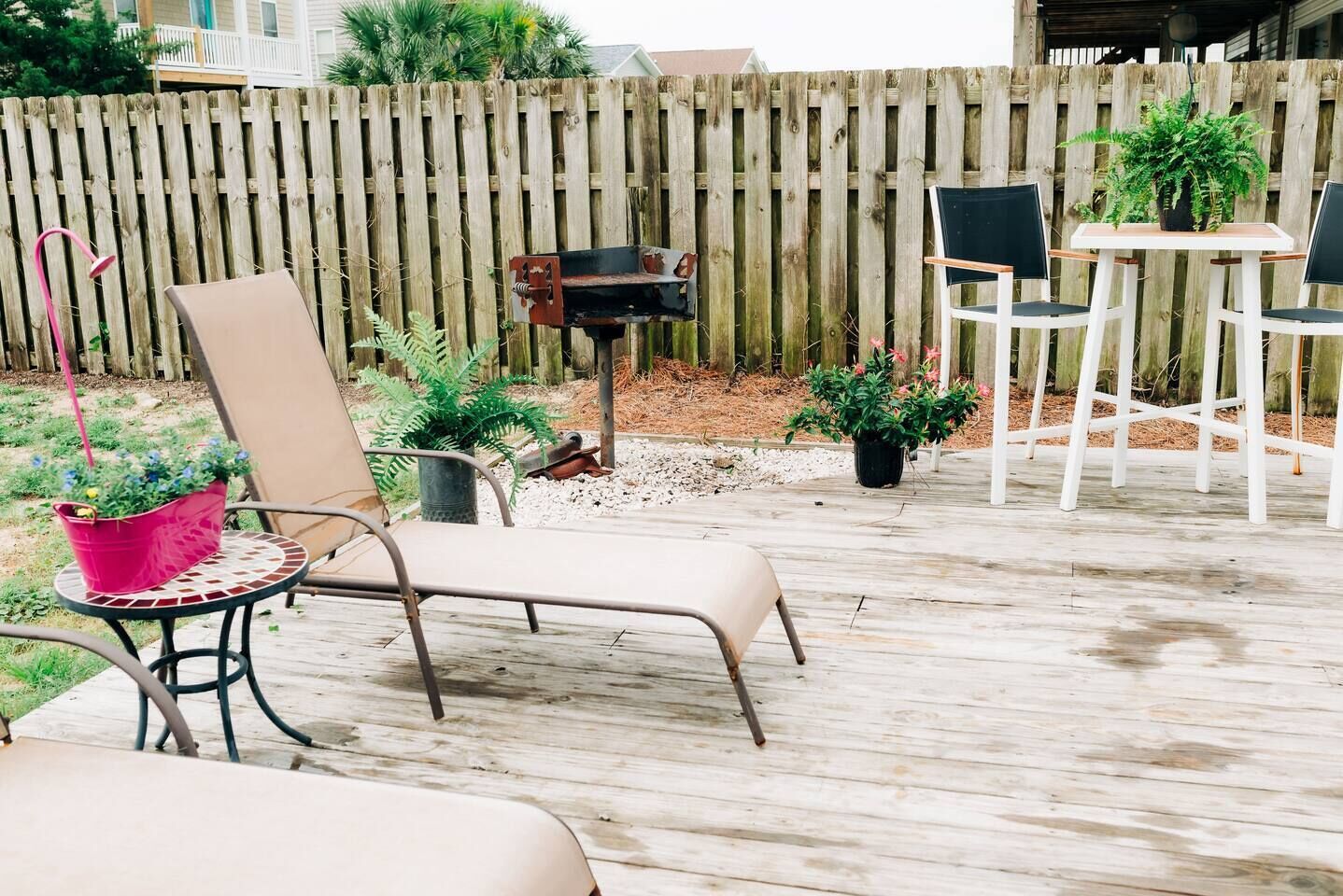 Une terrasse en bois, agrémentée de meubles d’extérieur, notamment une chaise et une table, entourée de plantes en pot et d’une clôture en bois.