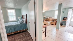 Une chambre à coucher avec un lit, un plancher en bois et une porte donnant sur un espace de vie comprenant un canapé et une table.
