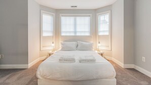 Un dormitorio ordenado con una cama grande, dos mesitas de noche y una ventana con persianas.