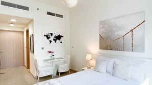 A modern hotel room with a large bed, a desk, and a chair. There is a world map and a tree branch artwork on the wall. - Premium Riviera Studio King Bed Pool & Gym (Dubai)