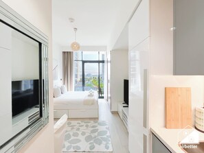 Ein modernes Hotelzimmer mit einem großen Bett, einem Fernseher, einem Balkon mit Stadtblick und einer Küchenzeile.