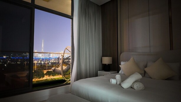 Hotelkamer met een groot bed, nachtkastje, lamp en uitzicht op een stadsbeeld met een brug en een toren.