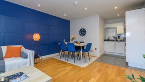 A modern living room with a blue accent wall, a dining area with blue chairs, and a kitchen with white cabinets. - Prime apartment in Leeds - Central location (Leeds)