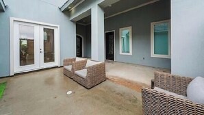 A covered outdoor area with a concrete floor, two wicker chairs, and a door leading to a building. - Gorgeous 7200 sq ft  estate with AC in vibrant Houston Galleria Area (Houston)