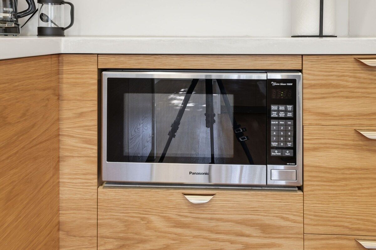 Een moderne keuken met een ingebouwde magnetron, houten kastjes en een roestvrijstalen aanrecht.