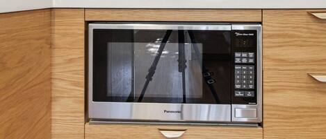 Een moderne keuken met een ingebouwde magnetron, houten kastjes en een roestvrijstalen aanrecht.