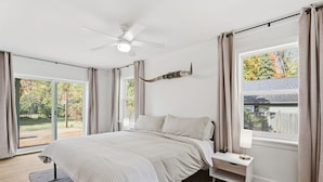 Une chambre à coucher avec un lit, une table de chevet, un ventilateur de plafond et une fenêtre avec des rideaux.