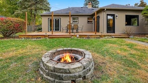 Une maison moderne avec un foyer extérieur dans le jardin, un patio couvert et une porte d’entrée dotée de panneaux de verre.