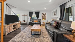 Ein modernes Wohnzimmer mit Flachbildfernseher, Ledersofas, einem Couchtisch und einem gemusterten Teppich.