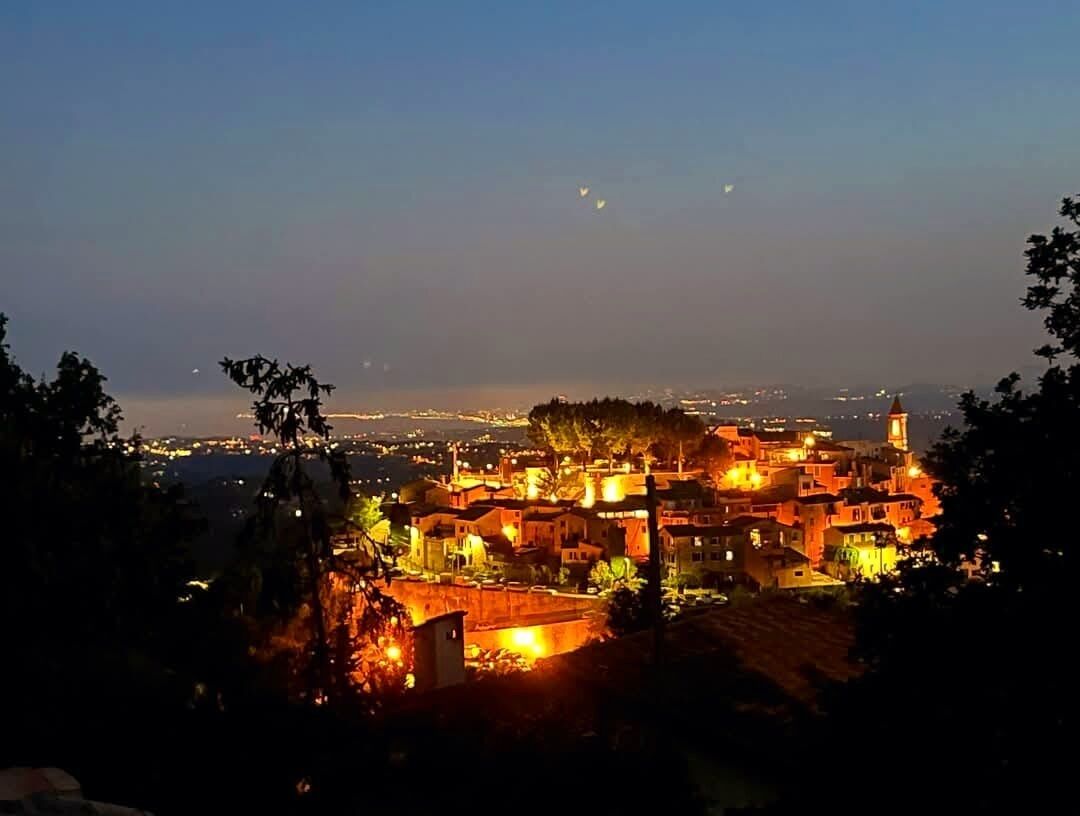 Une vue nocturne d’un village densément peuplé, caractérisé par une architecture traditionnelle et illuminé par des lampadaires et les lumières des bâtiments.