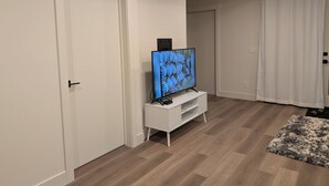 A modern living room with a flat-screen TV on a white stand, wooden flooring, and white walls.