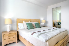 A neatly made bed with a wooden headboard, two bedside tables with lamps, a mirror, and a light-colored floor.