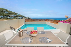A poolside table with a view of the ocean, a bottle of champagne, and a flower arrangement.