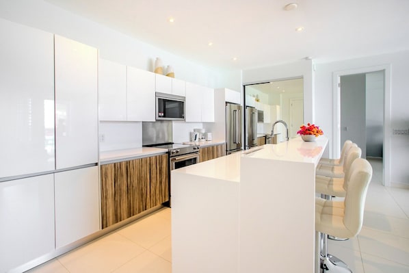 A modern kitchen with white cabinetry, stainless steel appliances, and a central island with bar stools.