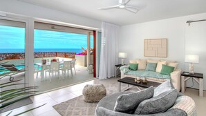 Ein modernes Wohnzimmer mit Balkon, Deckenventilator, einer Couch, einem Couchtisch und einem Essbereich mit Stühlen und Tisch.
