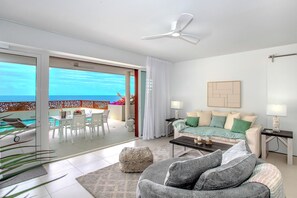Un salon moderne avec un balcon, un ventilateur de plafond, un canapé, une table basse et un coin repas comprenant des chaises et une table.