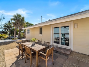 A patio with a wooden table and chairs, a potted plant, and a sliding glass door leading to an outdoor seating area. - Seahorse Cottage 2 - 2/2 with Private Beach (Englewood)