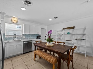 A modern kitchen with white cabinets, a wooden dining table, and a built-in shelf unit. - Seahorse Cottage 2 - 2/2 with Private Beach (Englewood)