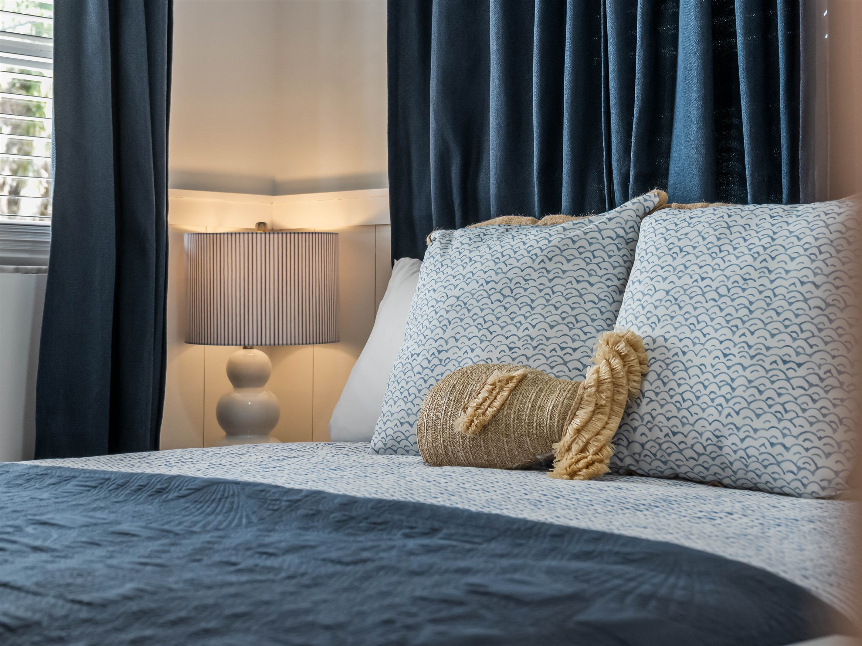 A bed with a blue and white patterned bedspread, two pillows with a wave design, and a textured throw pillow.