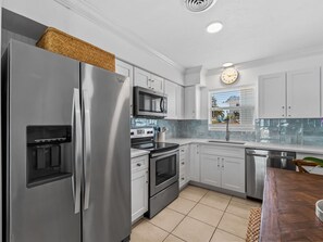 A modern kitchen with stainless steel appliances, white cabinetry, and a window with a view. - Seahorse Cottage 2 - 2/2 with Private Beach (Englewood)