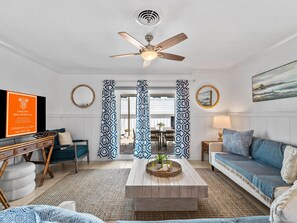 A living room with a ceiling fan, a television, a sofa, a coffee table with a plant, and patterned curtains. - Seahorse Cottage 2 - 2/2 with Private Beach (Englewood)