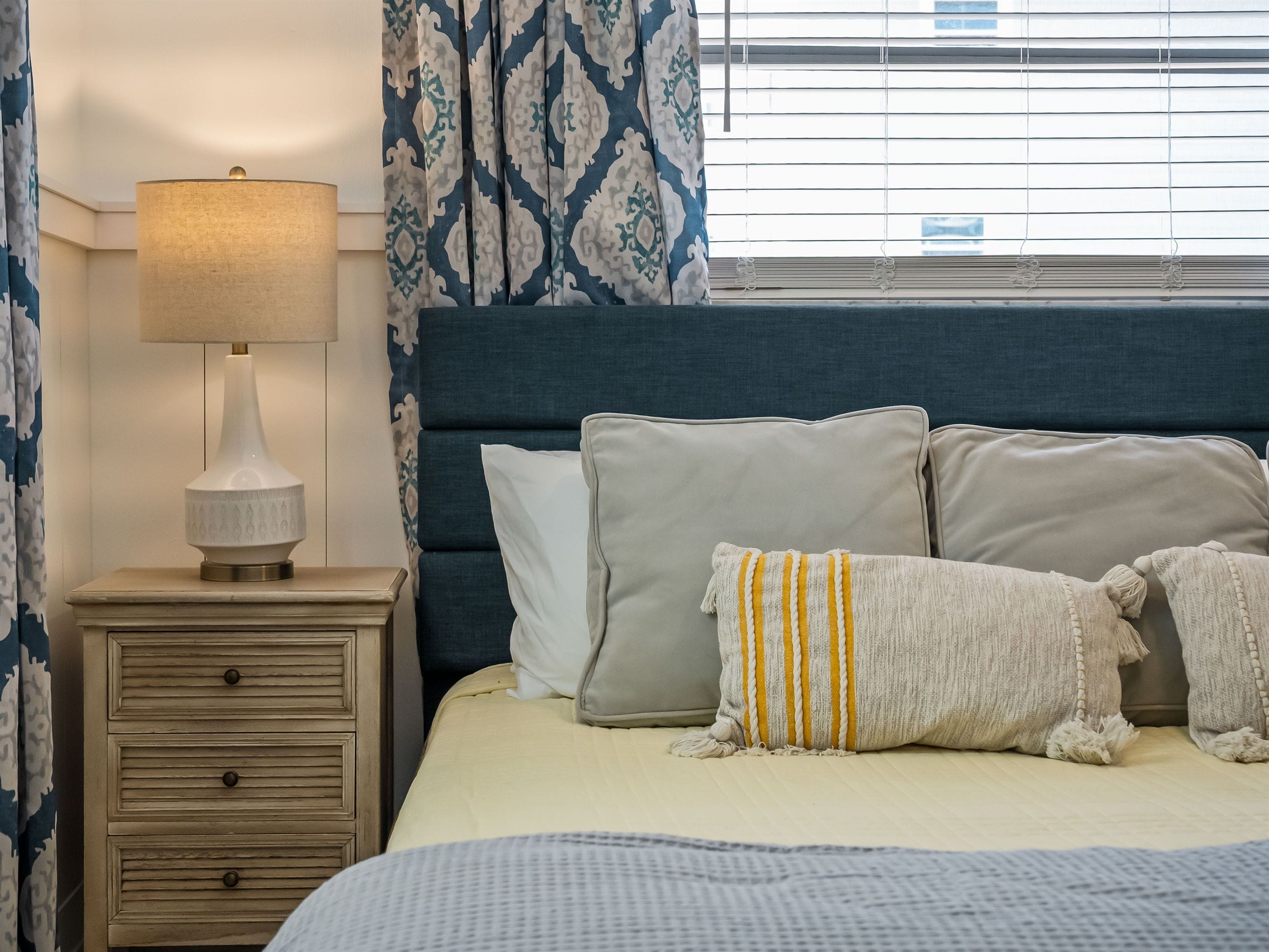 A neatly made bed with pillows, a bedside lamp, and a wooden nightstand.
