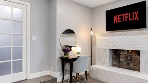 A modern living room with a fireplace, a mounted television displaying 'NETFLIX,' and a small table with a vase of flowers. - Bella| Pool/Spa|Downtown|Freeways|Beaches (San Diego)