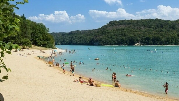 A beach with people swimming and sunbathing, surrounded by greenery and hills. - Gîte Les Plaisirs du Lac with spa & sauna (Charchilla)
