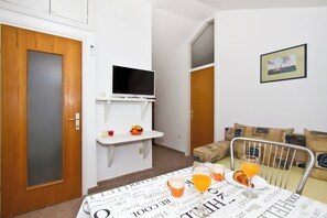 A small room with a wooden door, a television on a white stand, a table with breakfast items, and a sofa with cushions. - Best location in Vodice with sea view, apartment 3 (Vodice)