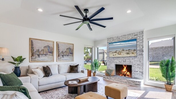 Una sala de estar moderna con chimenea, un ventanal grande y un ventilador de techo.
