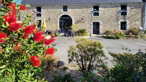 A stone building with a central arched entrance, multiple windows, and a paved courtyard. - La Maison Keribin 4****, Luxury traditional self catering cottage with its private Jacuzzi (Min stay 3 nights) (MOELAN SUR MER)