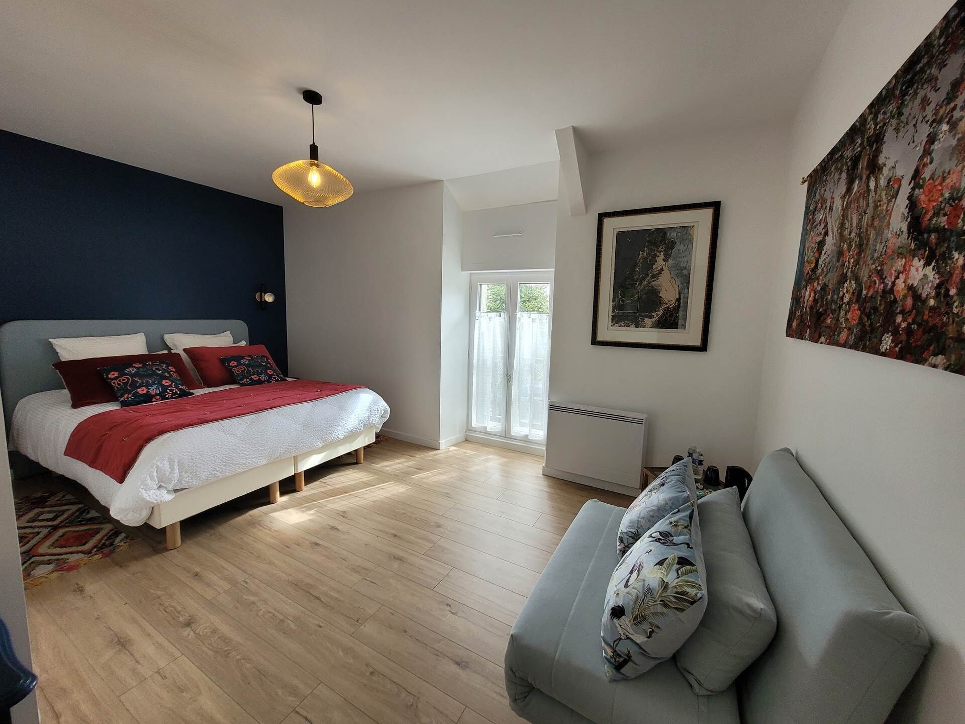 A modern bedroom with a bed, a sofa, a radiator, and a large window.