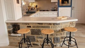 A kitchen with a central island, three bar stools, and pendant lighting. - La Maison Keribin 4****, Luxury traditional self catering cottage with its private Jacuzzi (Min stay 3 nights) (MOELAN SUR MER)