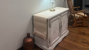 Huoneessa on valkoinen kaappi, lamppu, kehystetty kuva, puinen tuoli ja suuri pullo.