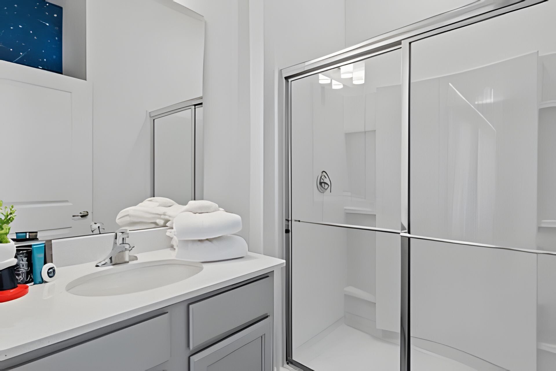 Une salle de bain moderne avec un grand miroir, un lavabo blanc et une cabine de douche en verre.
