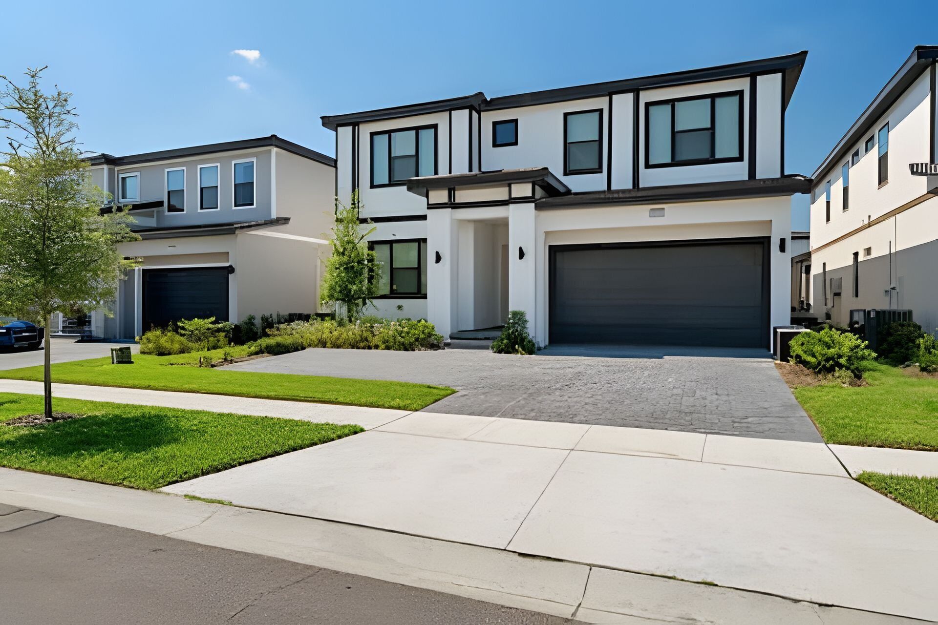 A modern two-story residential building with a central garage, a driveway, and well-maintained landscaping.