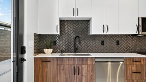 Et moderne køkken med hvide skabe, en backsplash i fiskebensmønster og en ståldiskmaskine.