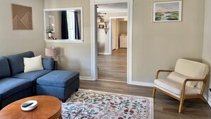 Una sala de estar con un sofá azul, una mesa de centro de madera, un sillón beige y un tapete floral.