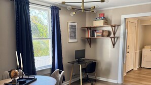 Una habitación moderna con una mesa de comedor, sillas, un escritorio con computadora, una estantería y un ventilador de techo.