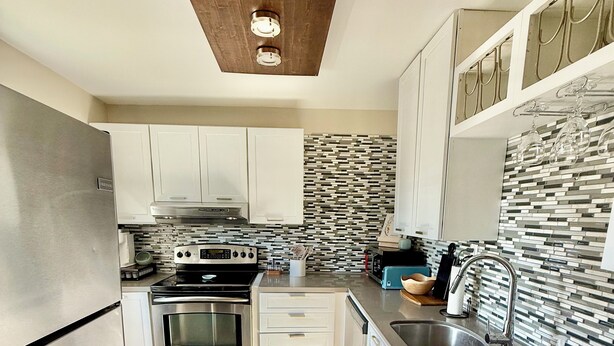 Una cocina moderna con electrodomésticos de acero inoxidable, armarios blancos, un salpicadero con diseño y techo de madera.