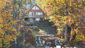 A cabin with a dock and kayaks by a lake surrounded by autumn trees. - 4BR Lakefront Home | Kayaks, Fire Pit & Views (Hawks)