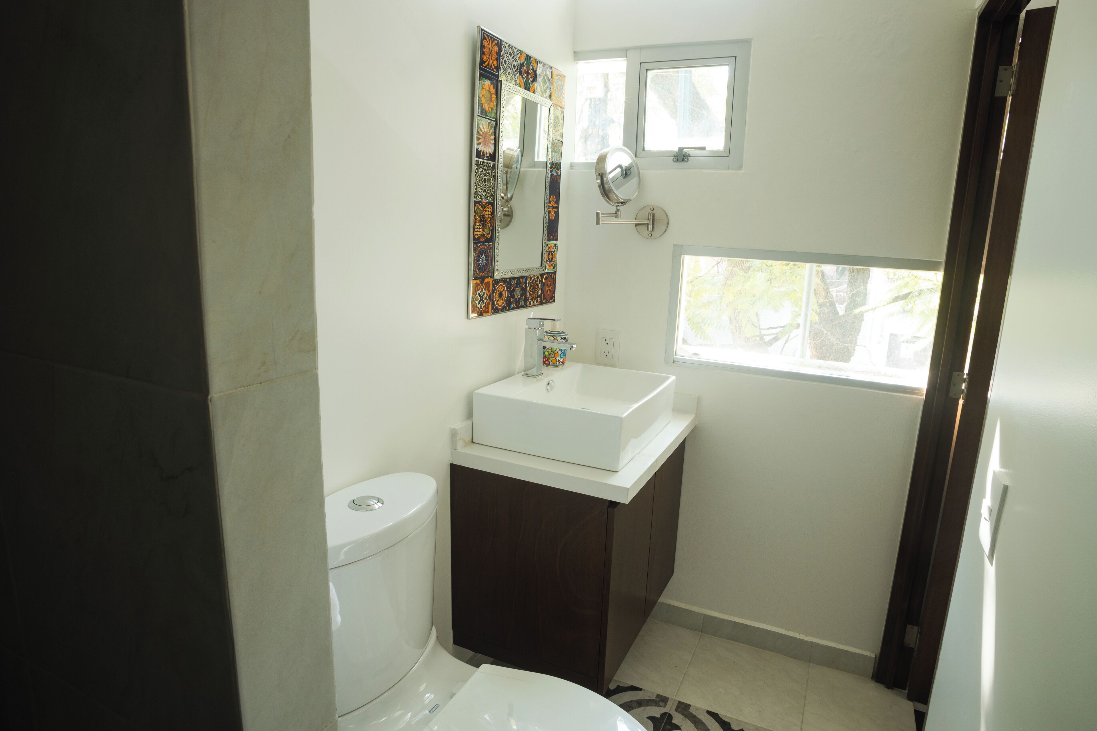 A bathroom with a toilet, sink, mirror, and window.