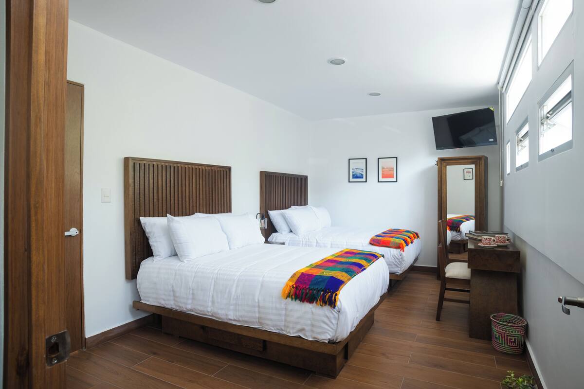 Un dormitorio con dos camas, un cabecero de madera, un televisor montado en la pared y un escritorio pequeño con una silla.