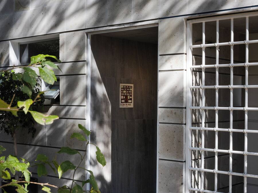 Una entrada de edificio con una reja metálica, una puerta con un letrero y una planta al frente.