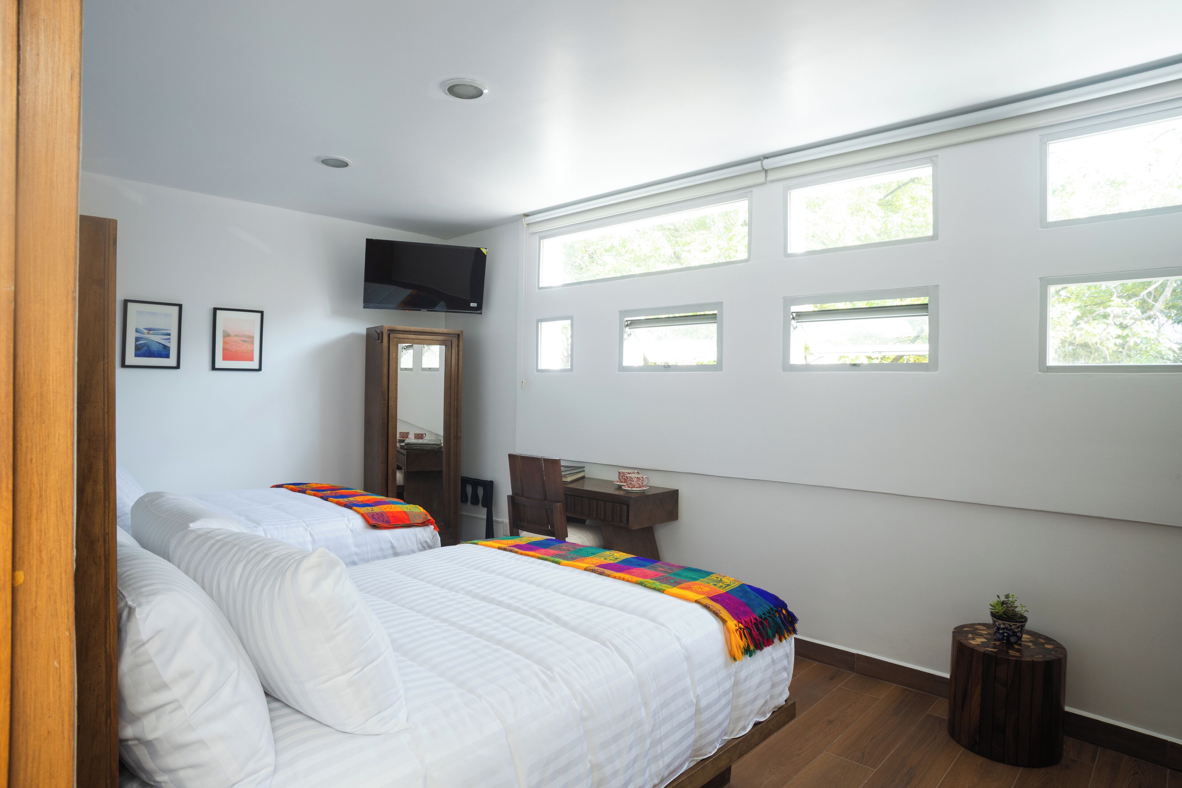 A bedroom with two beds, a TV, a desk, and multiple windows.
